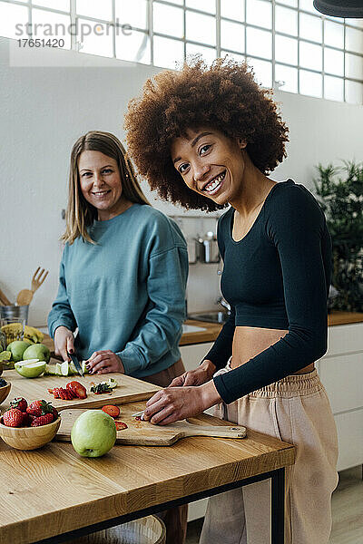 Glückliche junge Frau mit Freundin  die zu Hause in der Küche Früchte schneidet