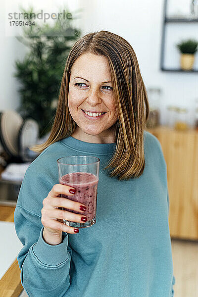 Glückliche Frau hält ein Glas Smoothie in der heimischen Küche