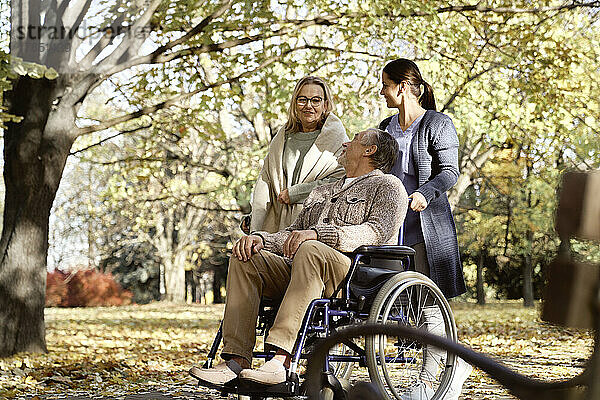 Lächelnder behinderter Mann mit Krankenschwester blickt ältere Frau an  die im Park spricht