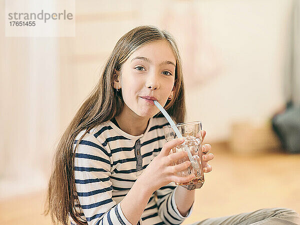 Mädchen trinkt ein Glas Wasser und sitzt zu Hause auf dem Boden