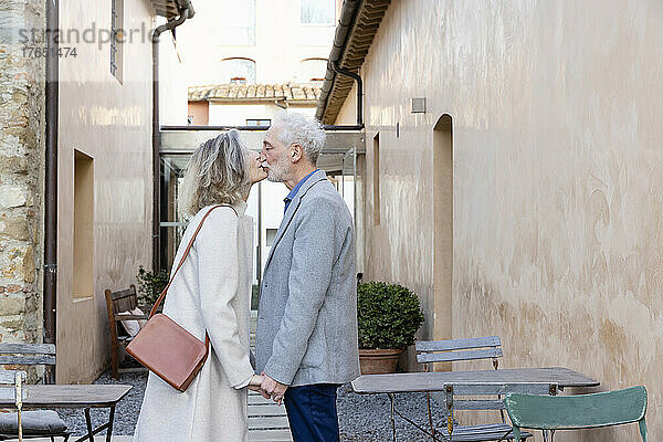 Liebevolles älteres Paar  das Händchen hält und sich im Innenhof des Hotels küsst