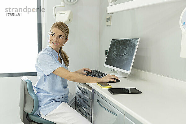 Zahnarzt sitzt auf einem Stuhl mit Computer auf dem Schreibtisch in der Zahnklinik