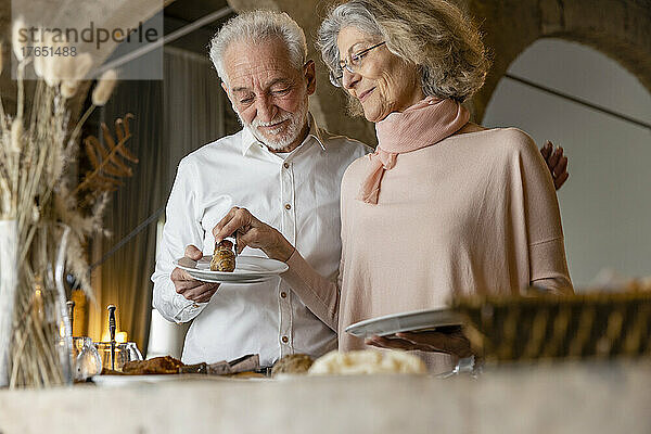 Lächelnde ältere Frau gibt einem Mann  der am Frühstücksbuffet im Boutique-Hotel steht  ein Croissant