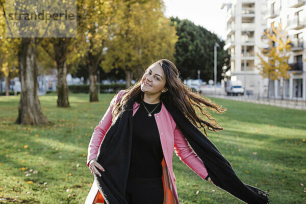 Lächelnde Frau genießt an einem sonnigen Tag den öffentlichen Park