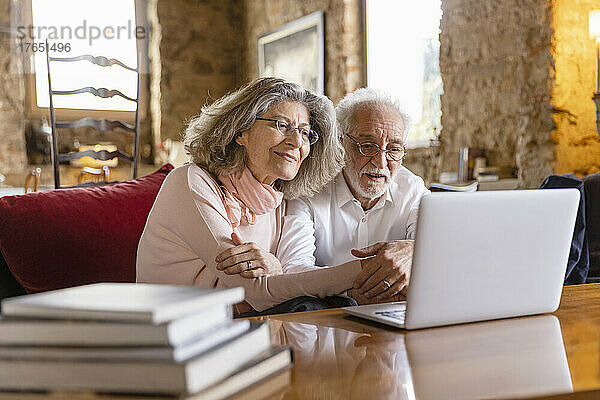 Lächelndes älteres Paar schaut auf den Laptop und sitzt auf dem Sofa im Boutique-Hotel