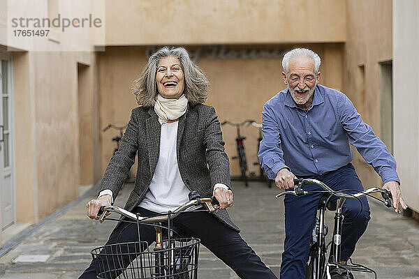 Glückliches älteres Paar  das vor dem Gebäude Fahrrad fährt