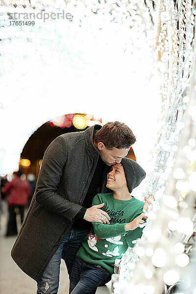 Father kissing son in tunnel with Christmas lights