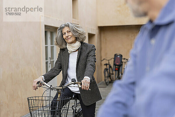 Lächelnde ältere Frau mit Fahrrad blickt Mann vor Gebäude an