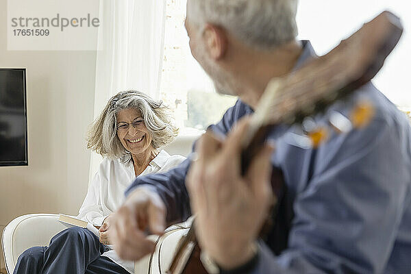 Glückliche Frau schaut Mann zu  der zu Hause Gitarre spielt