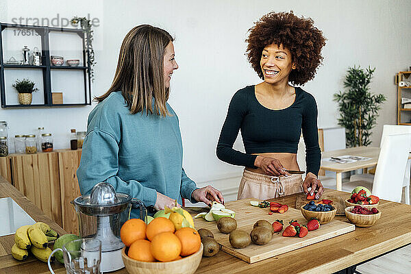 Fröhliche Freunde schneiden frisches Obst und reden zu Hause in der Küche miteinander