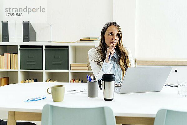 Geschäftsfrau mit der Hand am Kinn sitzt am Schreibtisch im Büro