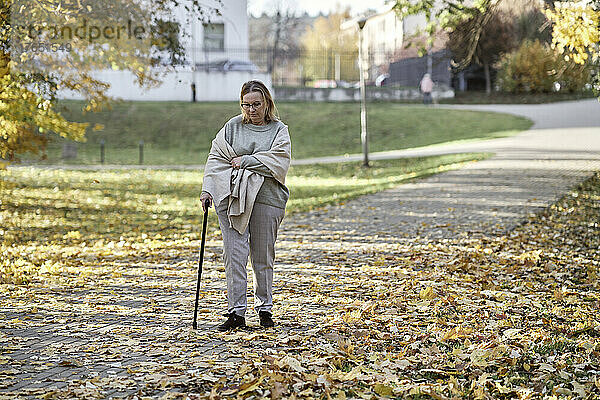 Ältere Frau geht mit Stock auf Fußweg im Park