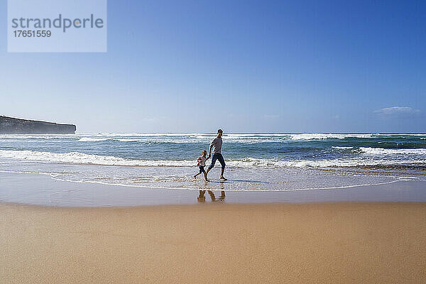 Vater und Tochter laufen an einem sonnigen Tag am Strand