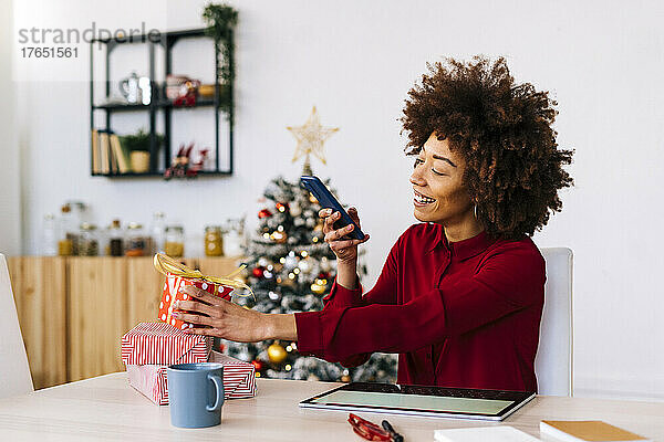 Glückliche Frau  die zu Hause Weihnachtsgeschenke mit dem Handy fotografiert