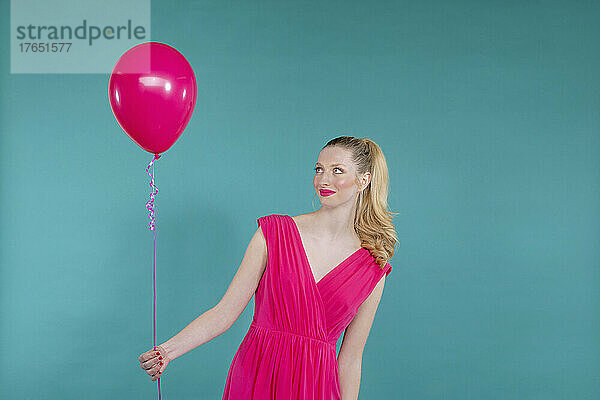 Smiling young woman holding pink balloon standing against green background