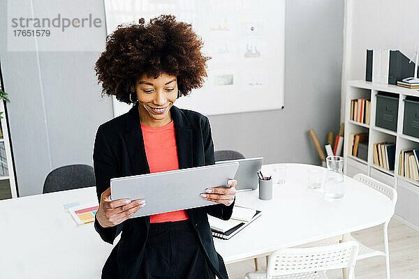 Lächelnde junge Geschäftsfrau mit Afro-Frisur mit Tablet-PC im Büro