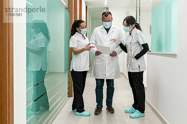 Arzt bespricht medizinischen Bericht mit Krankenschwestern im Flur des Krankenhauses