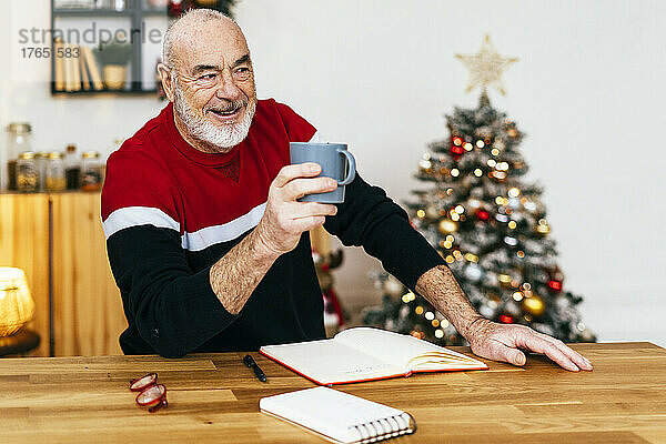 Lächelnder älterer Mann mit Kaffeetasse am Tisch sitzend