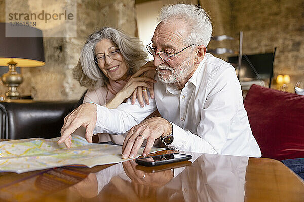 Smiling senior man pointing at map sitting by woman on sofa at boutique hotel
