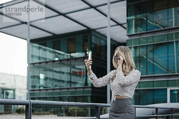 Geschäftsfrau macht Selfie mit Smartphone vor Bürogebäude
