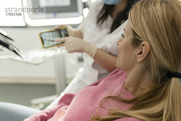Zahnarzt erklärt Patienten in Zahnklinik das Röntgenbild auf dem Mobiltelefon