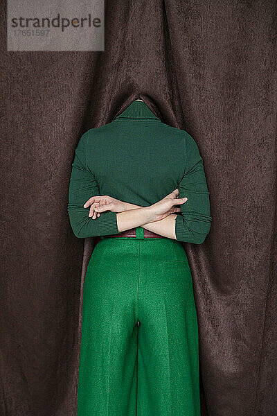 Woman with arms crossed behind back hiding head in curtain