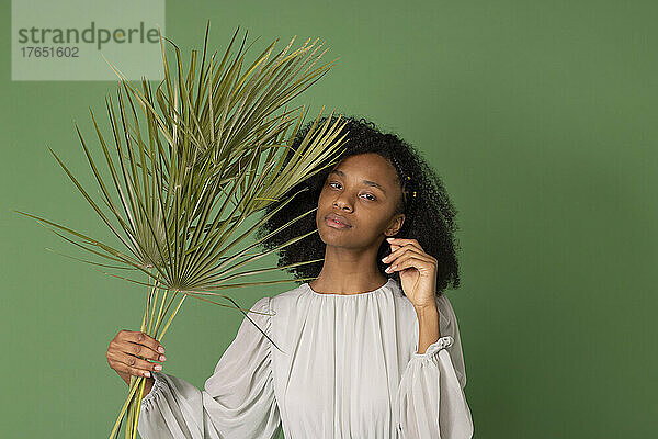 Junge Frau hält Palmzweige vor grünem Hintergrund
