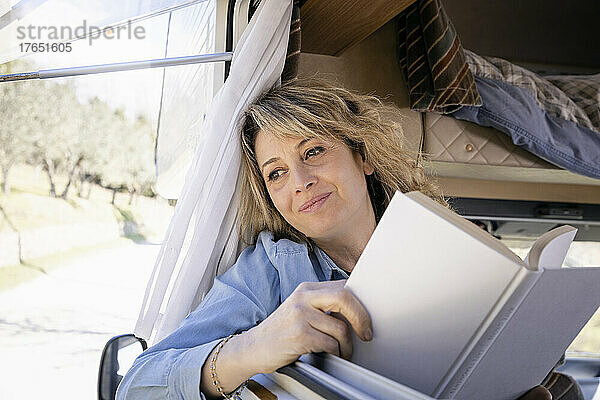 Nachdenkliche Frau mit Buch  die aus dem Fenster des Wohnmobils schaut