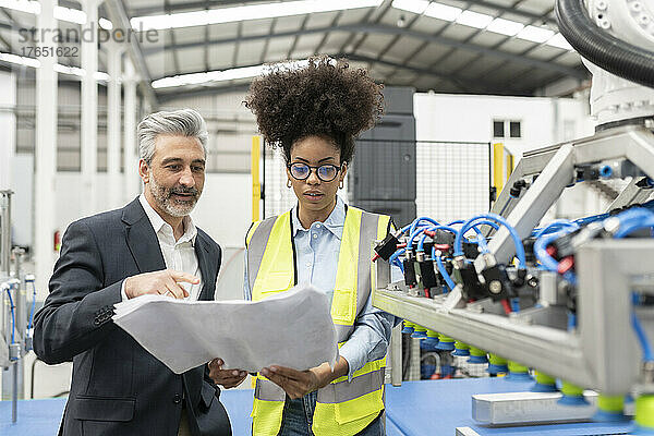 Geschäftsmann diskutiert mit Ingenieur in Fabrik über Bauplan