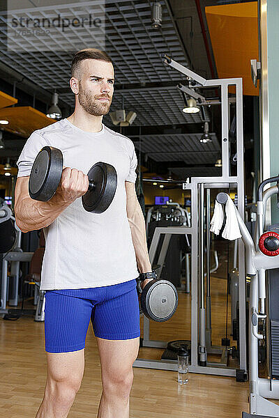 Junger Mann hebt im Fitnessstudio Hanteln