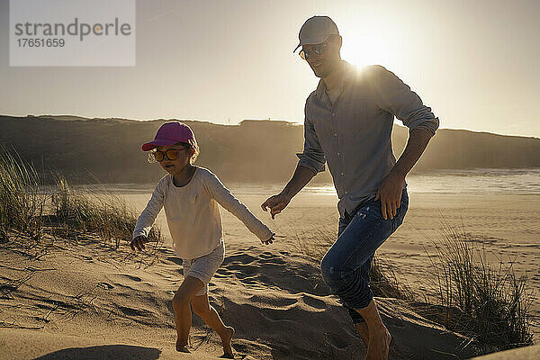 Glücklicher Vater mit Tochter  die bei Sonnenuntergang auf Sand läuft