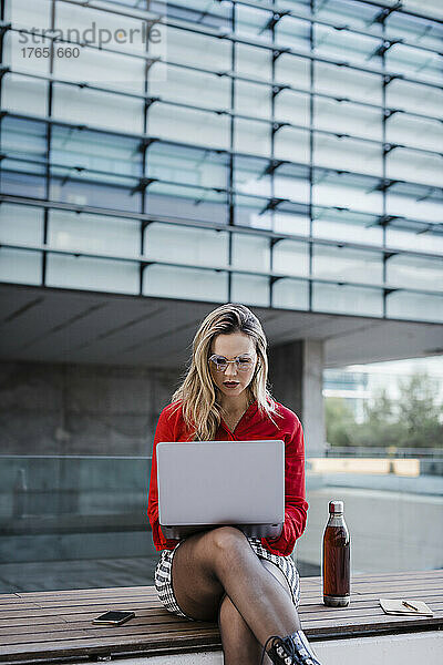 Geschäftsfrau benutzt Laptop auf Bank sitzend