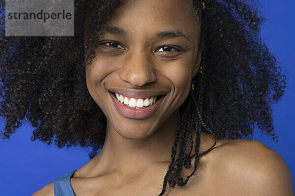 Glückliche junge Frau mit Afro-Frisur vor blauem Hintergrund
