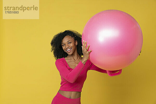 Lächelnde Frau mit rosa Luftballon vor gelbem Hintergrund