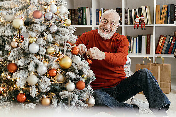 Lächelnder älterer Mann schmückt zu Hause den Weihnachtsbaum