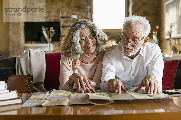 Lächelnde Frau und Mann  die auf dem Sofa im Boutique-Hotel sitzen und auf den Stadtplan schauen