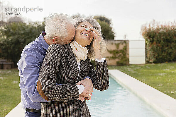 Älterer Mann umarmt fröhliche Frau vor Schwimmbad