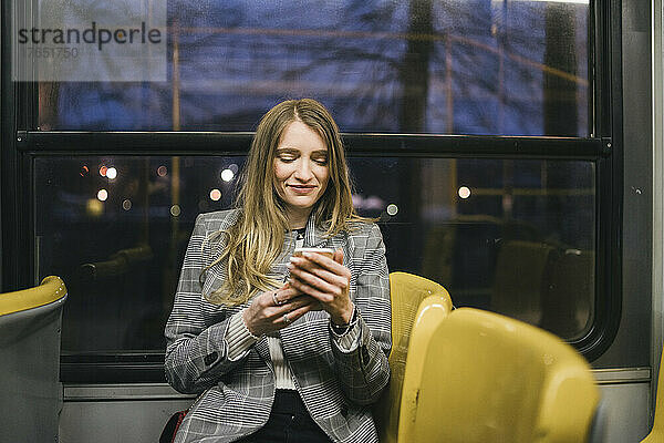 Lächelnde Frau  die in der Straßenbahn ihr Smartphone benutzt