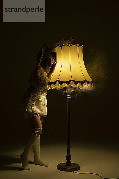 Junge Frau im Kaninchenkostüm lehnt an beleuchteter Lampe im dunklen Raum