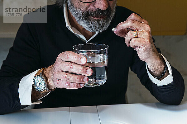 Älterer Mann hält ein Glas Wasser am Tisch