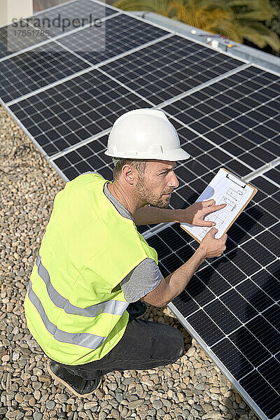 Ingenieur untersucht Sonnenkollektoren mit Blaupause an einem sonnigen Tag