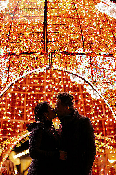 Couple kissing on mouth in front of Christmas lights