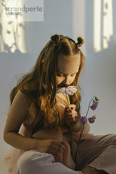 Mädchen riecht frische Blumen und sitzt vor einer weißen Wand