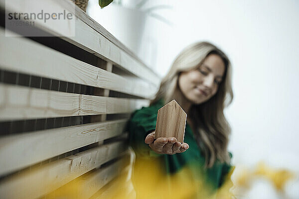 Lächelnde Frau zeigt ein Holzhausmodell  das zu Hause sitzt