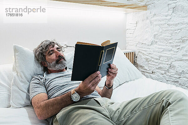 Älterer Mann liest ein Buch  das zu Hause im Bett liegt