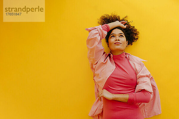 Beautiful woman with hand raised lying on yellow background