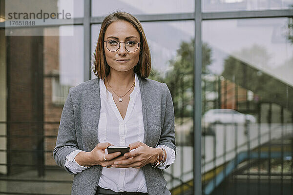 Junge Frau mit Mobiltelefon steht vor Gebäude