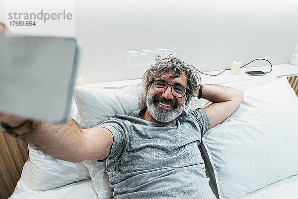 Glücklicher Mann  der zu Hause im Bett ein Selfie mit dem Smartphone macht