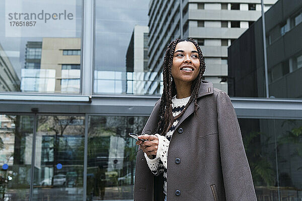 Lächelnde Geschäftsfrau im Blazer mit Smartphone im Büropark