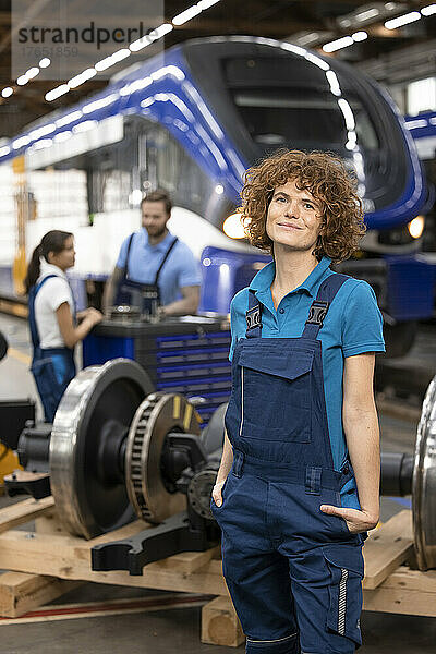 Lächelnder Ingenieur steht mit den Händen in den Taschen in der Industrie